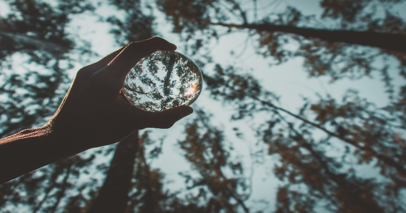 Mano sujetando una bola de cristal reflectante en un bosque.